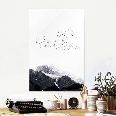 Glasbild - Vogelschwarm vor Bergen Schwarz Weiß - Hochformat 3:2